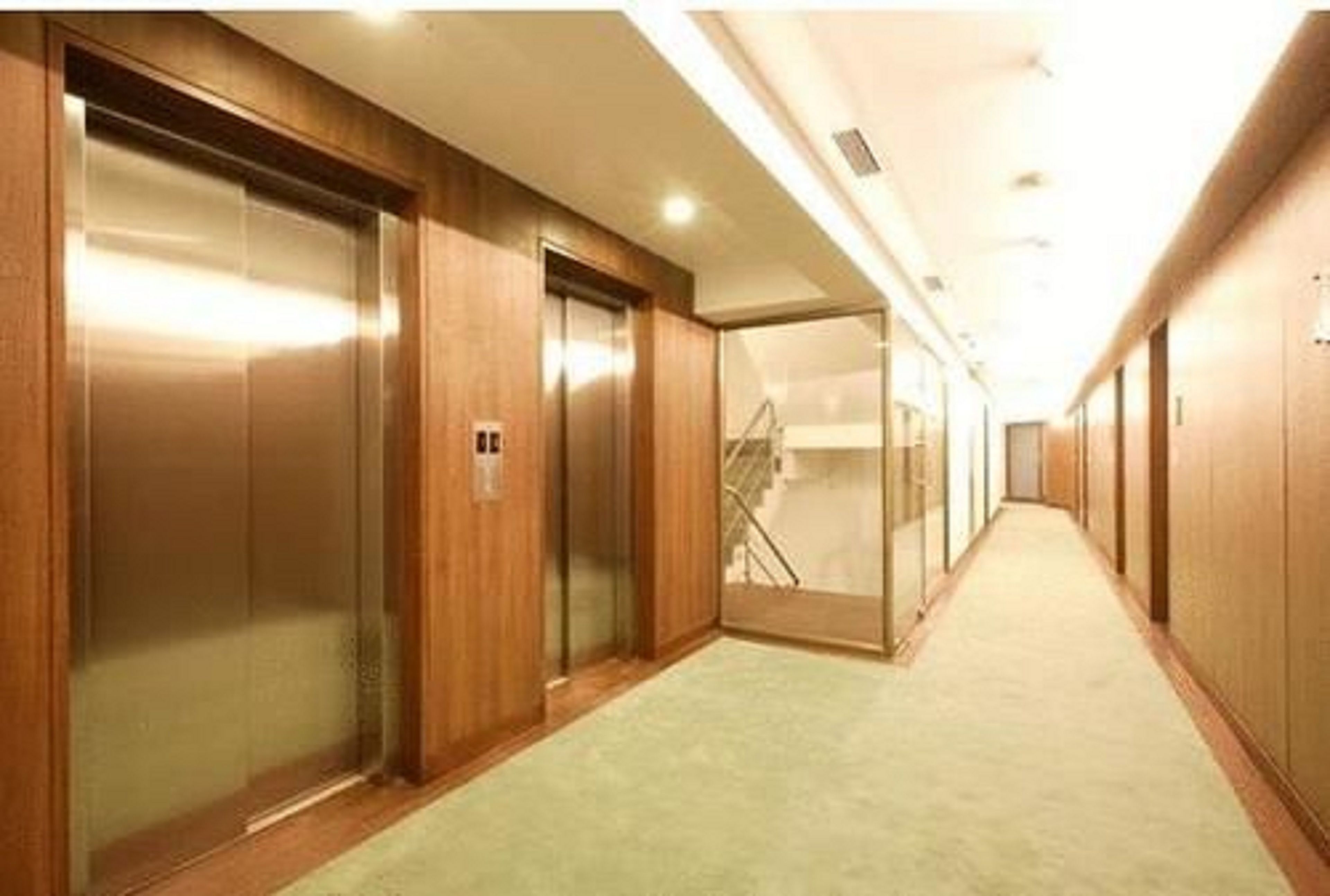 A hotel corridor with wooden walls, a carpeted floor, and an elevator.