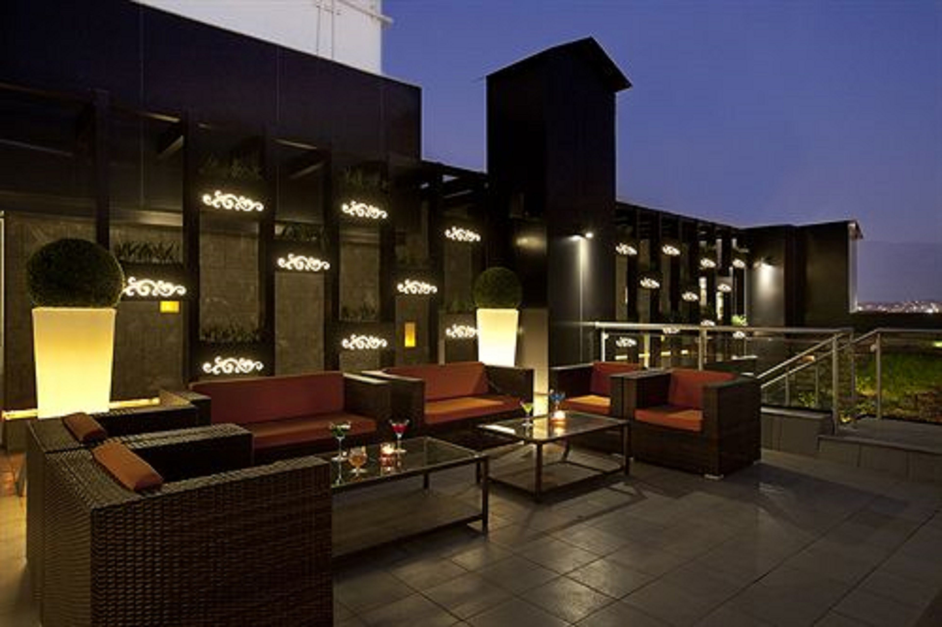An outdoor seating area with wicker furniture and a glass coffee table, illuminated by ambient lighting.