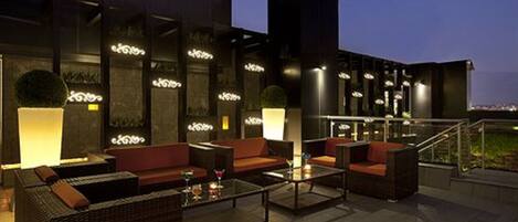 An outdoor seating area with wicker furniture and a glass coffee table, illuminated by ambient lighting.