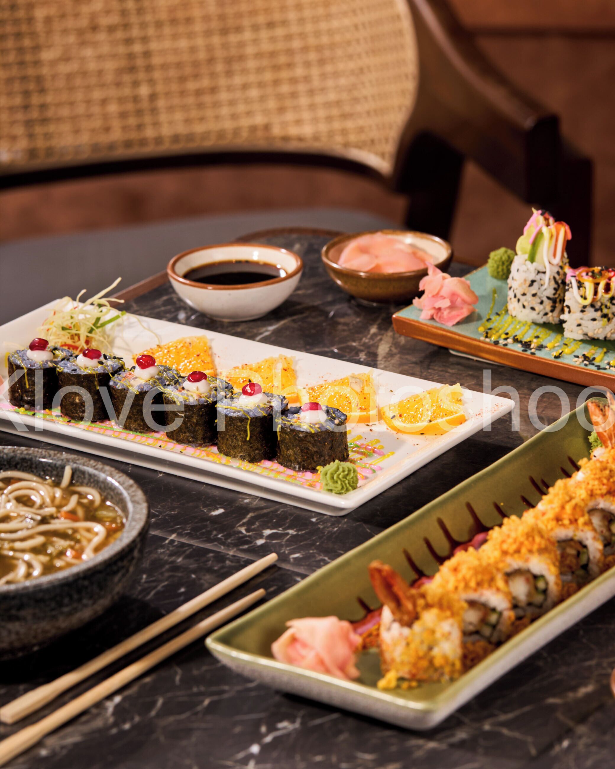 Variedad de platos de sushi sobre una mesa de mármol, con palillos y recipientes con salsa.