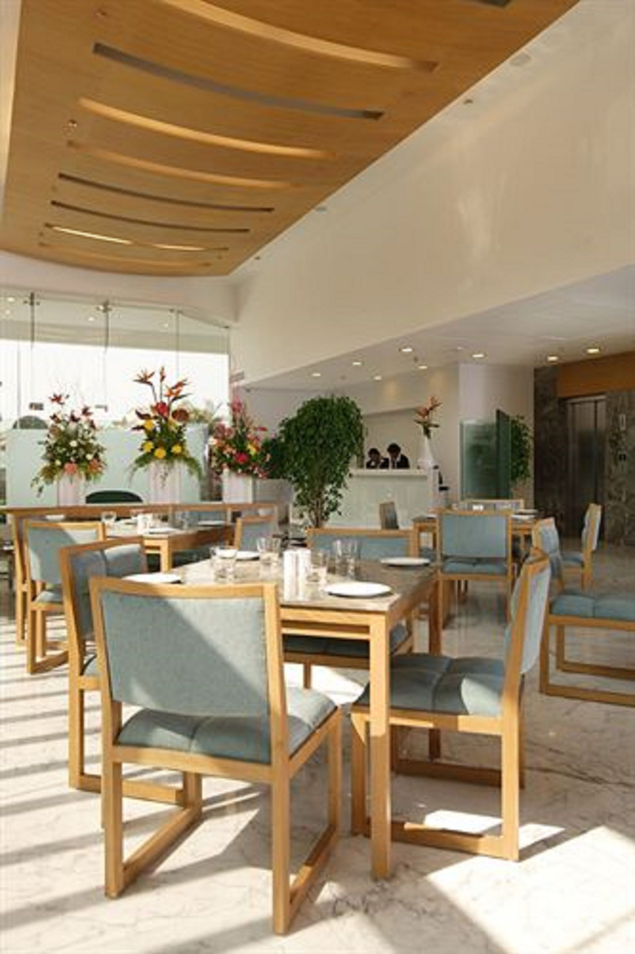 A modern dining area with wooden tables and chairs, a reception desk, and decorative plants.