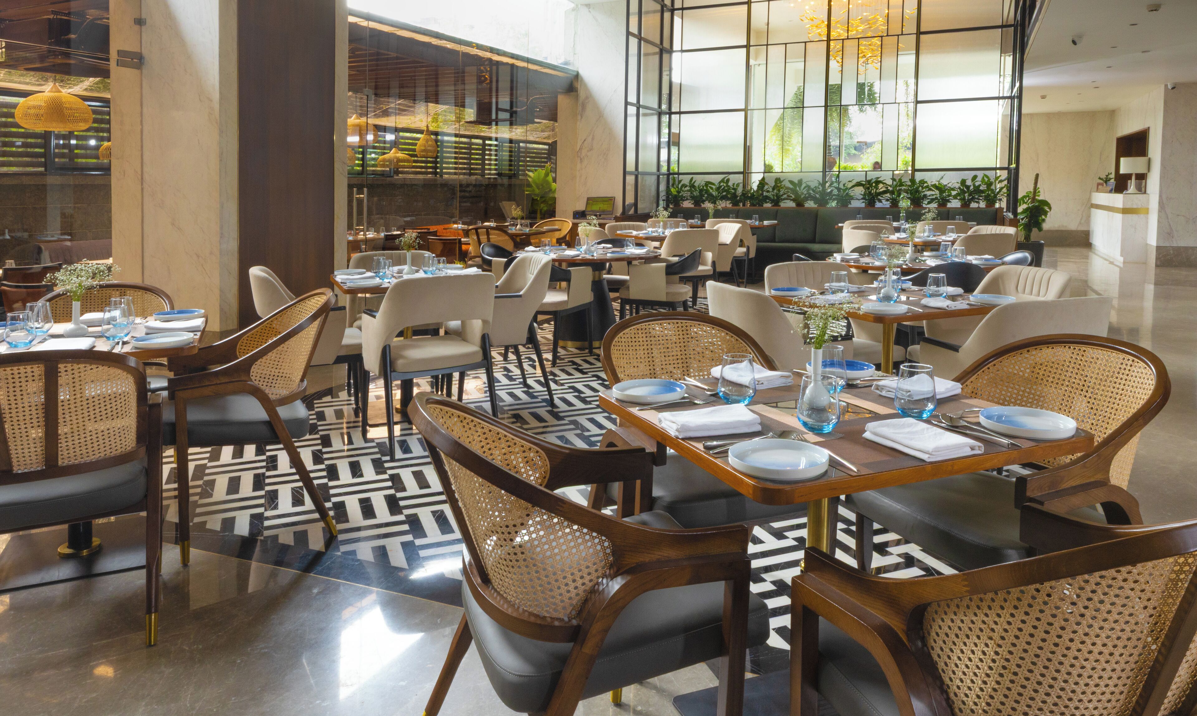 En rummelig restaurant med højt til loftet, store vinduer og moderne indretning. Bordene er pænt anrettet med stole, og gulvet har et geometrisk mønster.