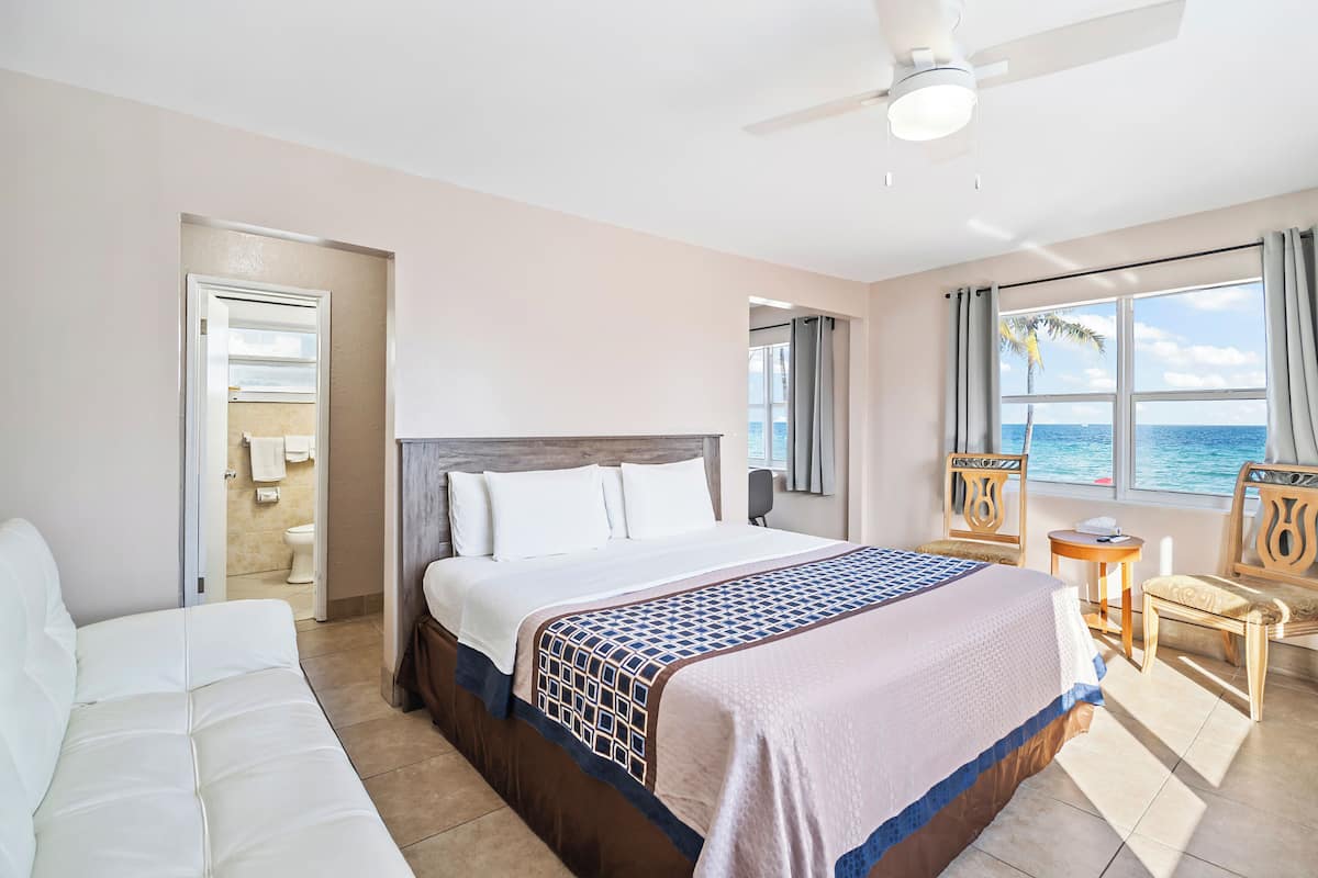 A hotel room with a bed, a chair, a small table, and a view of the sea.