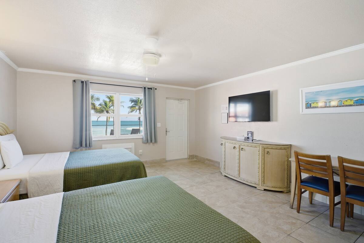 A hotel room with two beds, a television, a cabinet, and a view of the ocean.