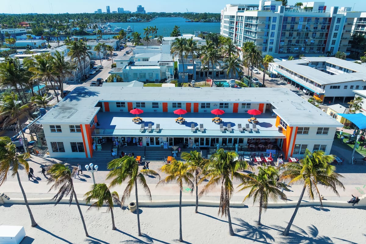 A beachfront hotel with multiple floors, outdoor seating with umbrellas, and a view of the ocean.