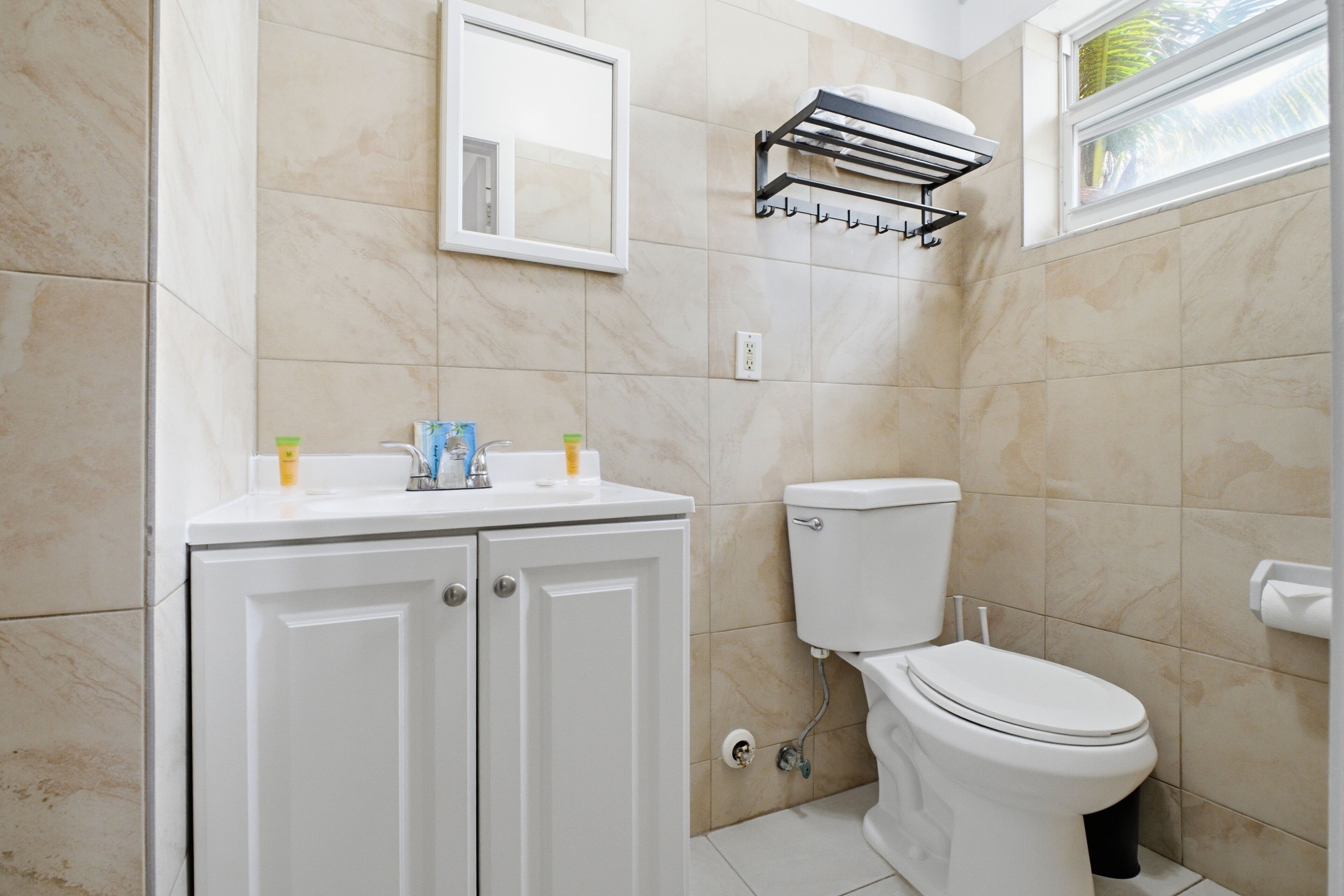 A bathroom with a toilet, a sink, cabinets, a towel rack, and a mirror.