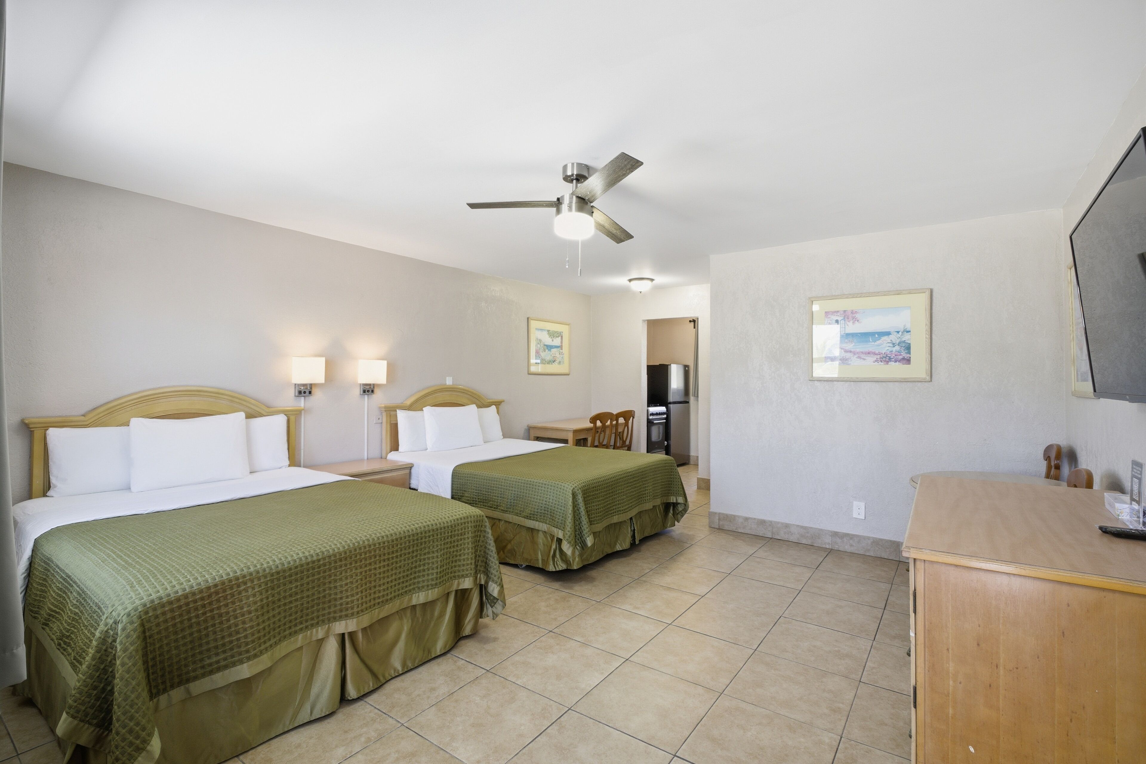 A hotel room with two beds, a desk, a chair, a television, and a ceiling fan.