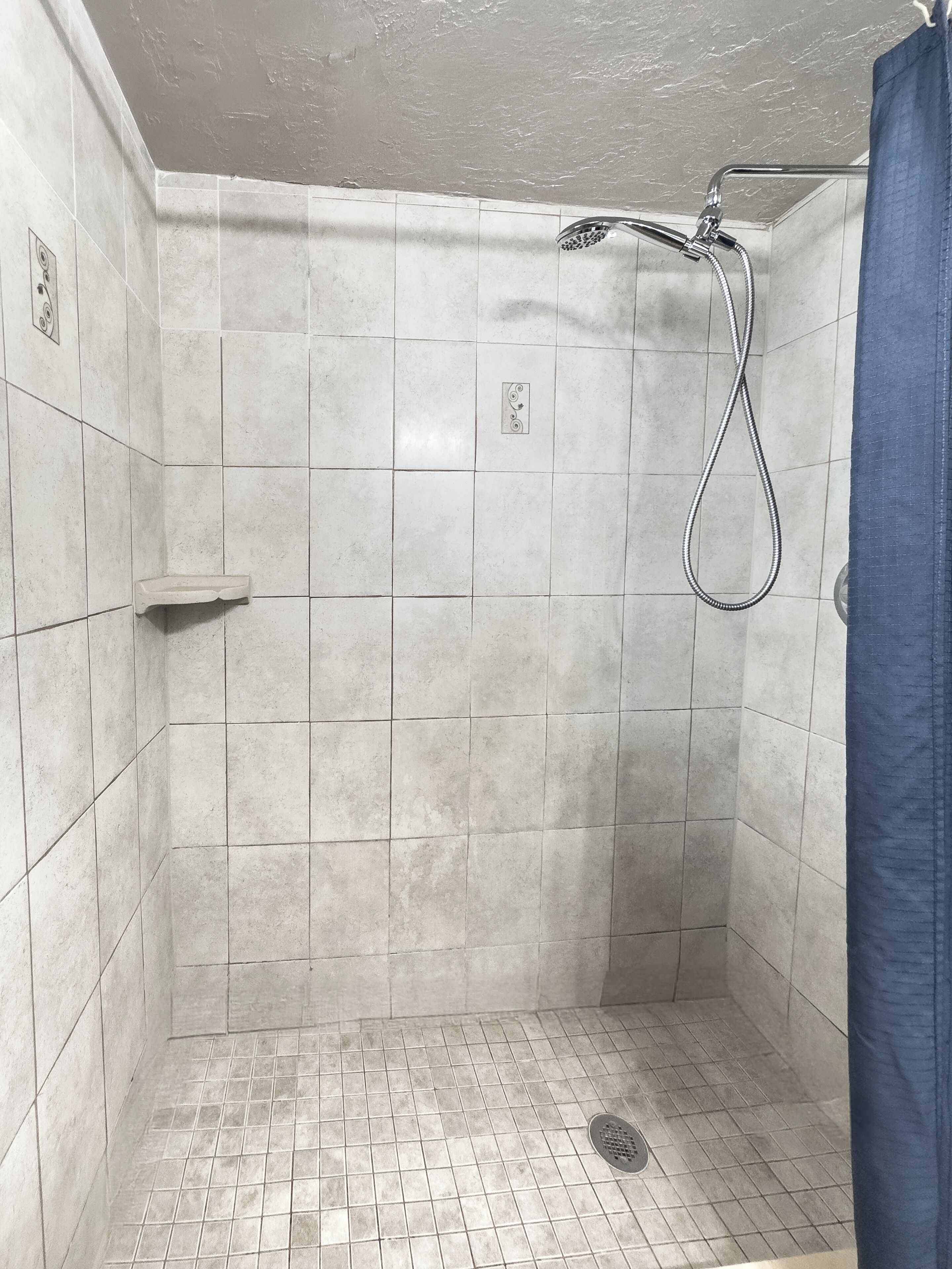 A small, tiled shower room with a showerhead and a drain.