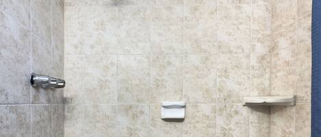 A small, tiled shower room with a handheld showerhead, a handheld faucet, and a built-in shelf.