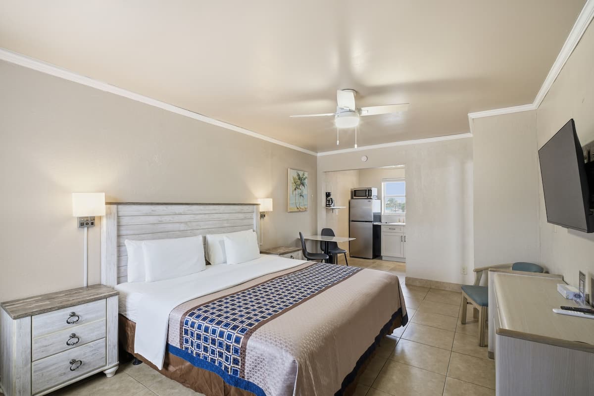 A hotel room with a bed, bedside table, desk, and kitchenette.