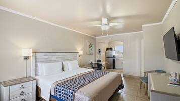 A hotel room with a bed, bedside table, desk, and kitchenette.