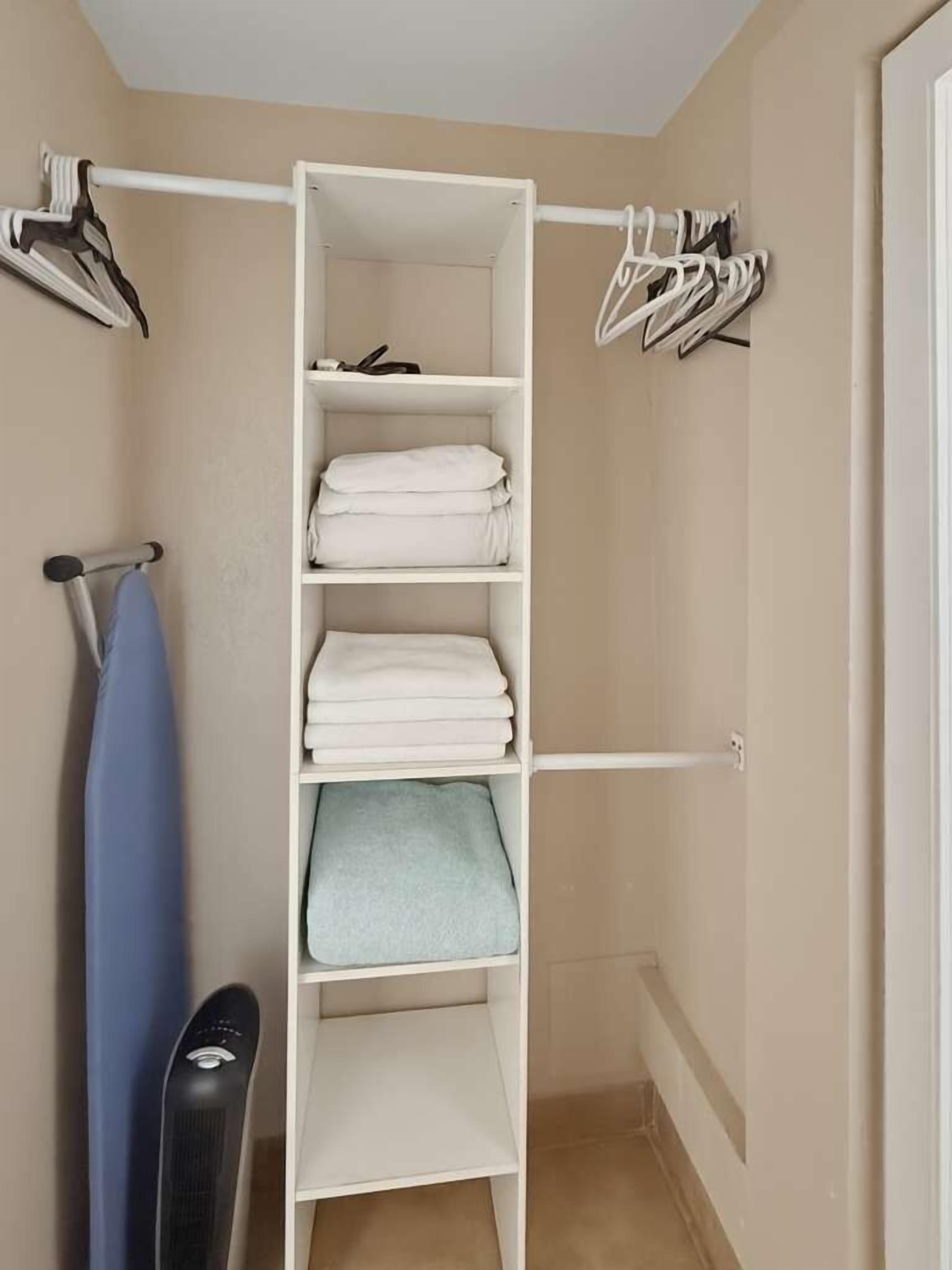 A walk-in closet with multiple shelves, a hanging rod, and a blue ironing board.