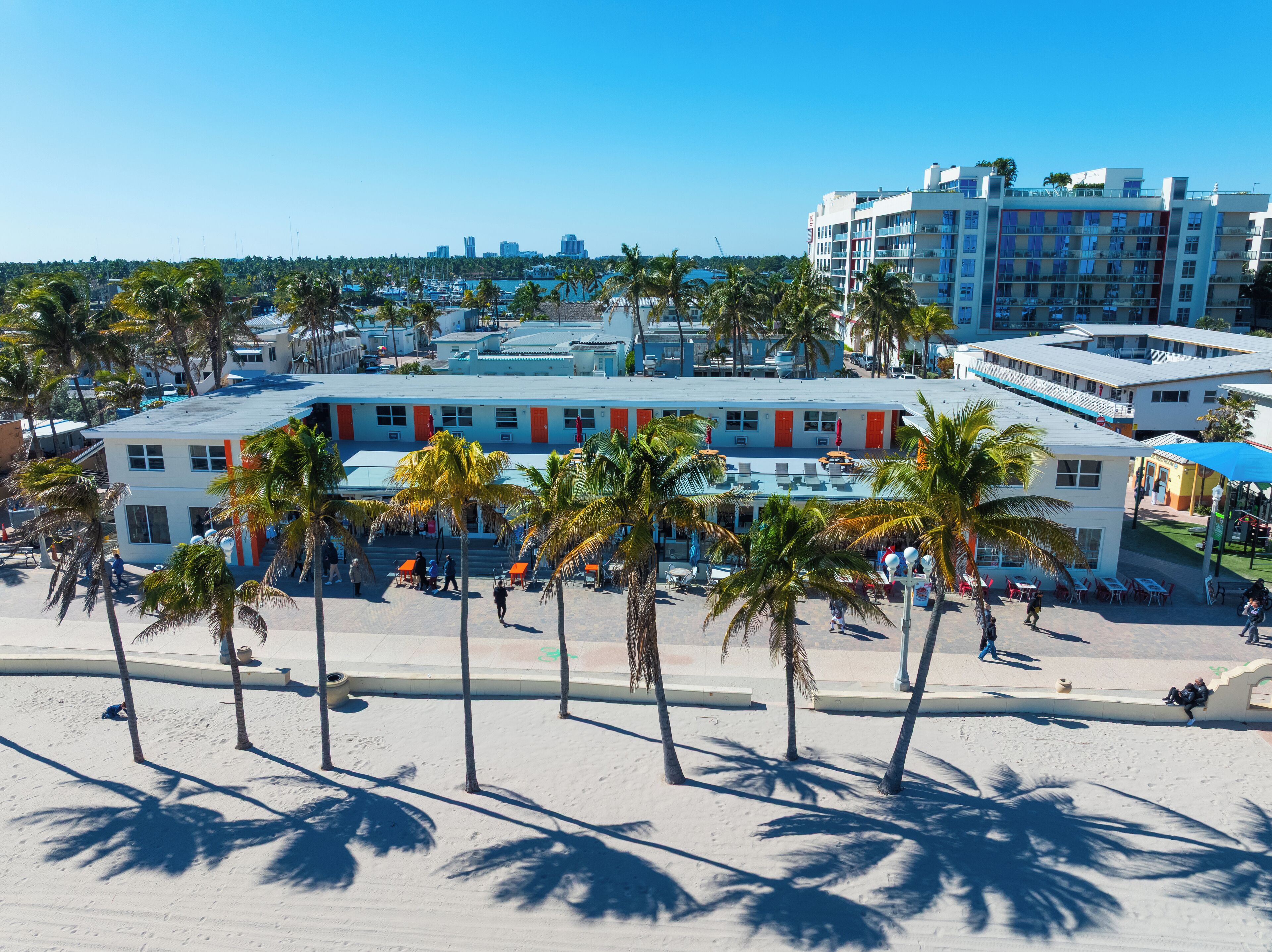 A beachfront hotel with multiple floors, palm trees, and a marina in the background.