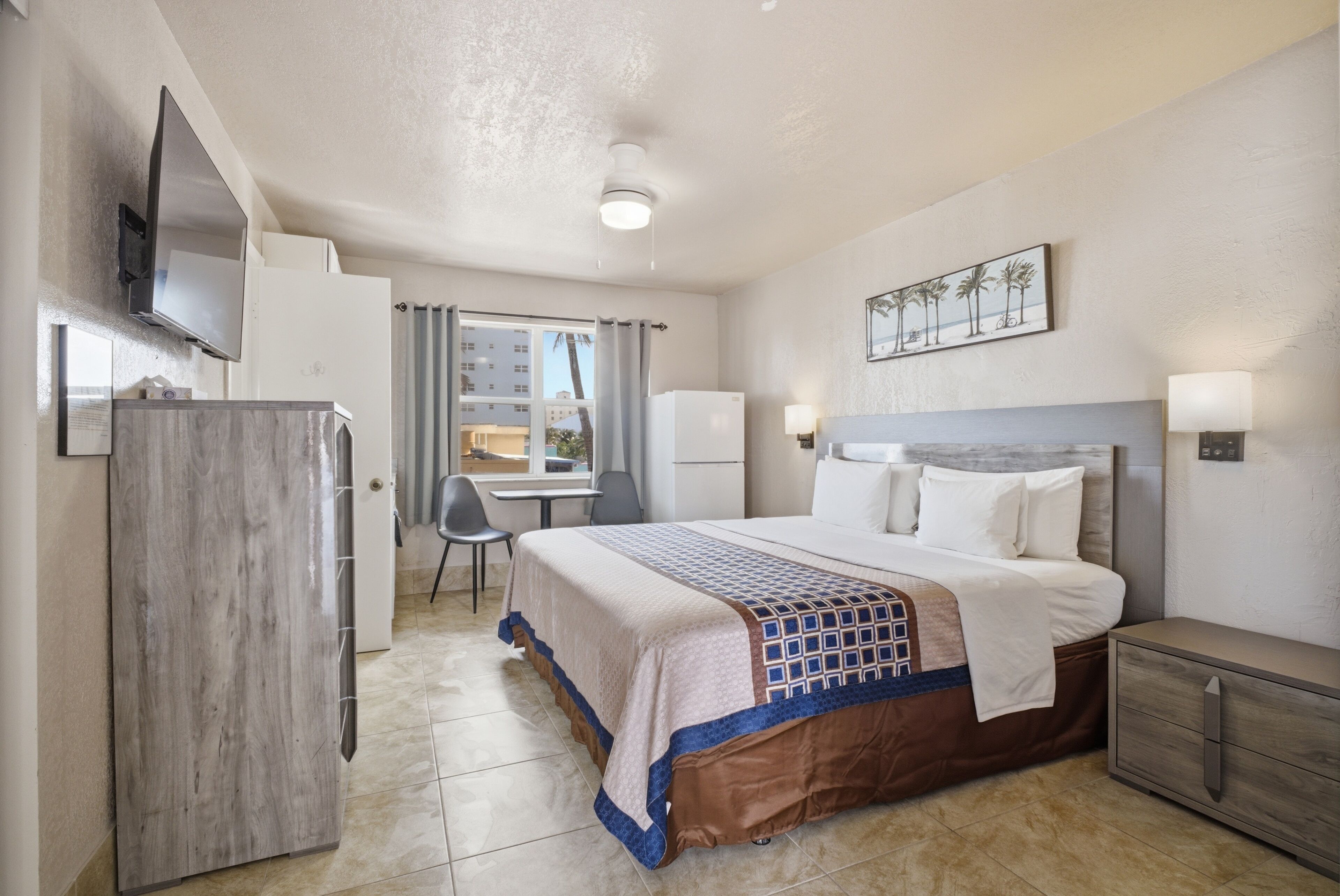 Habitación de hotel con cama, escritorio, televisor y ventana con cortinas.