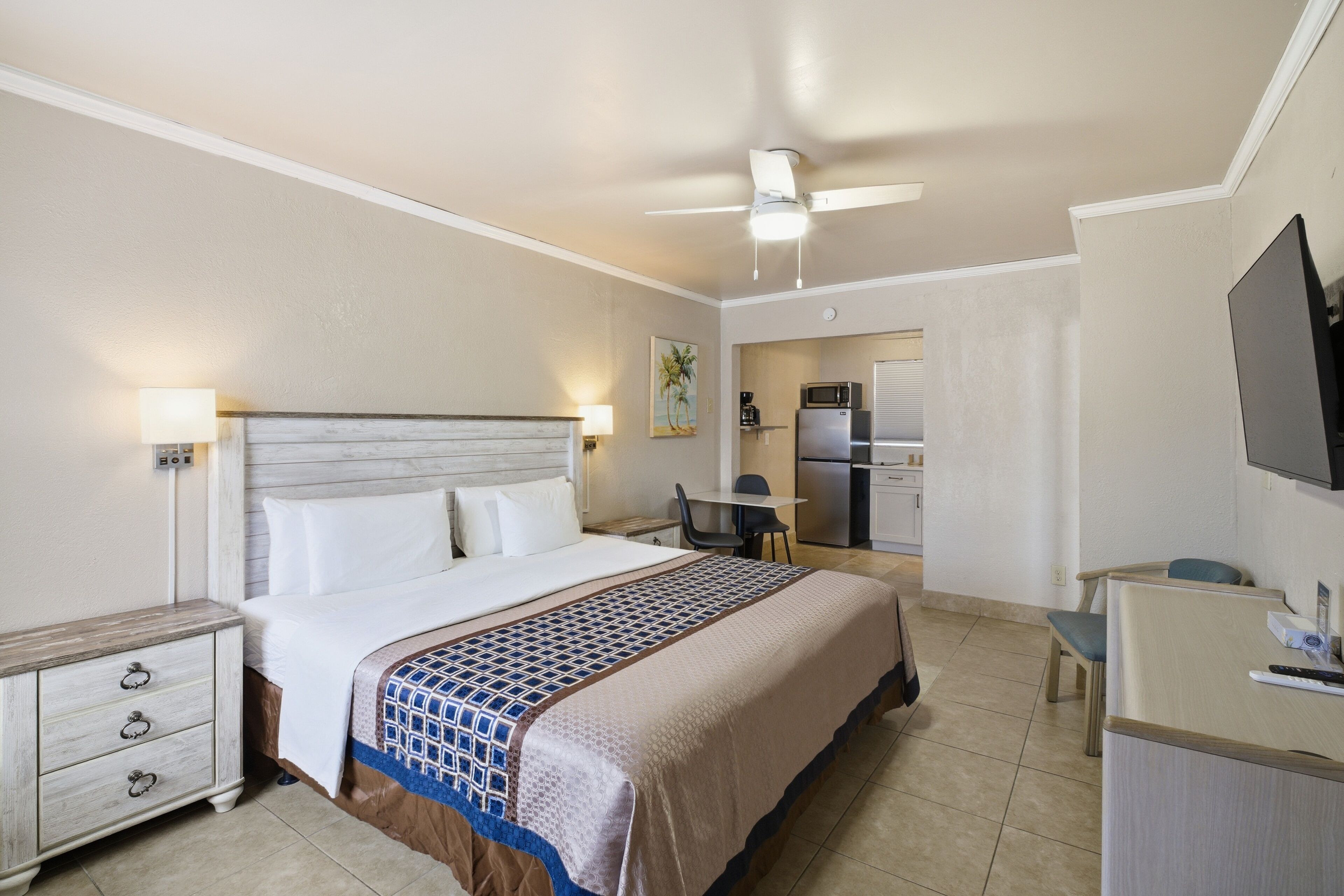 A hotel room with a bed, a desk, a chair, a television, and a kitchenette.