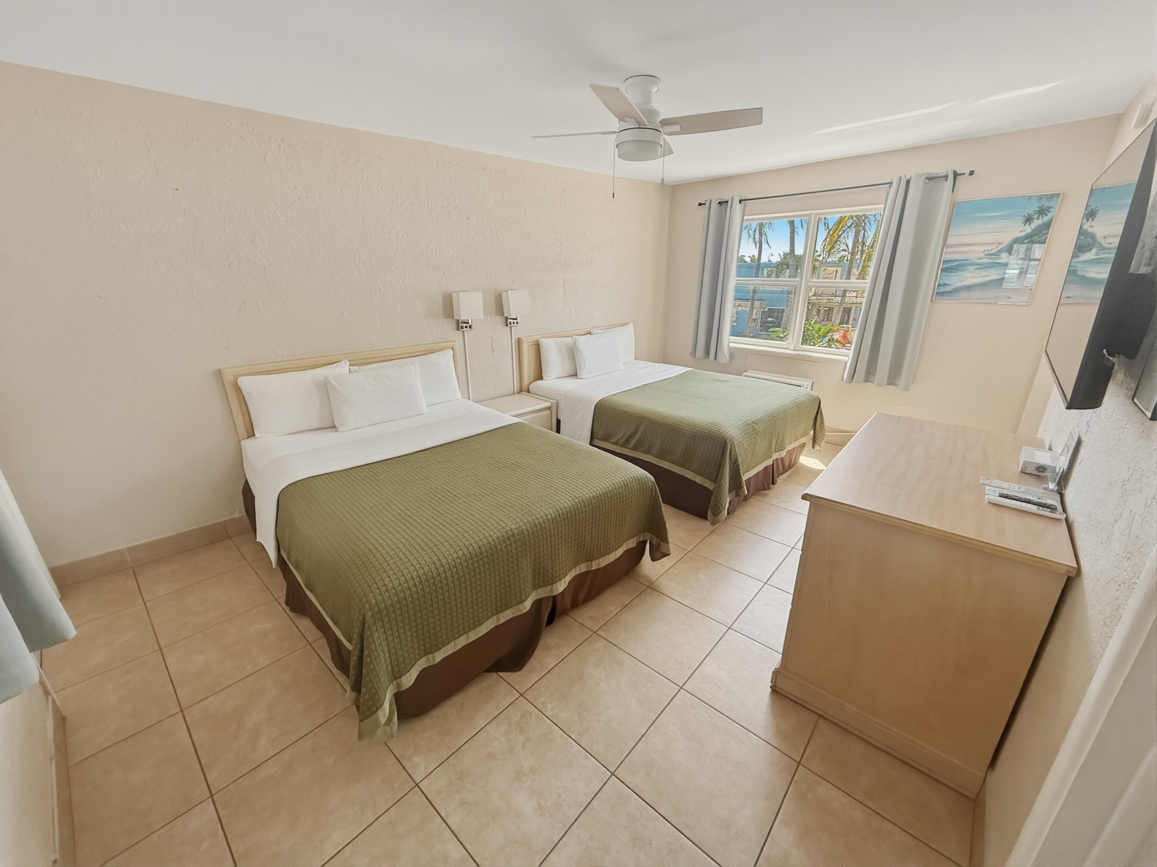 Une chambre d’hôtel avec deux lits, un ventilateur de plafond, une fenêtre avec des rideaux et un bureau.