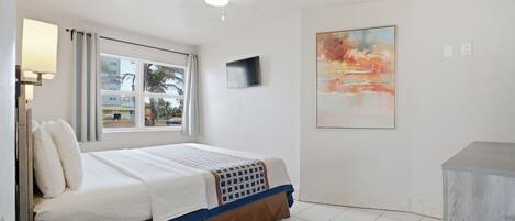 Une chambre d’hôtel avec un lit, un ventilateur de plafond, une télévision, un tableau et une fenêtre avec des rideaux.