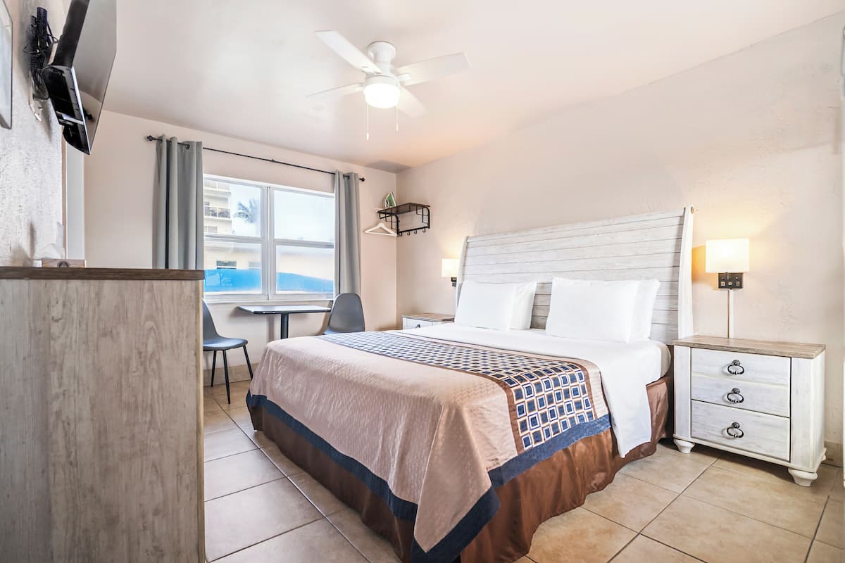A hotel room with a bed, bedside table, desk, chair, and a view of the ocean.