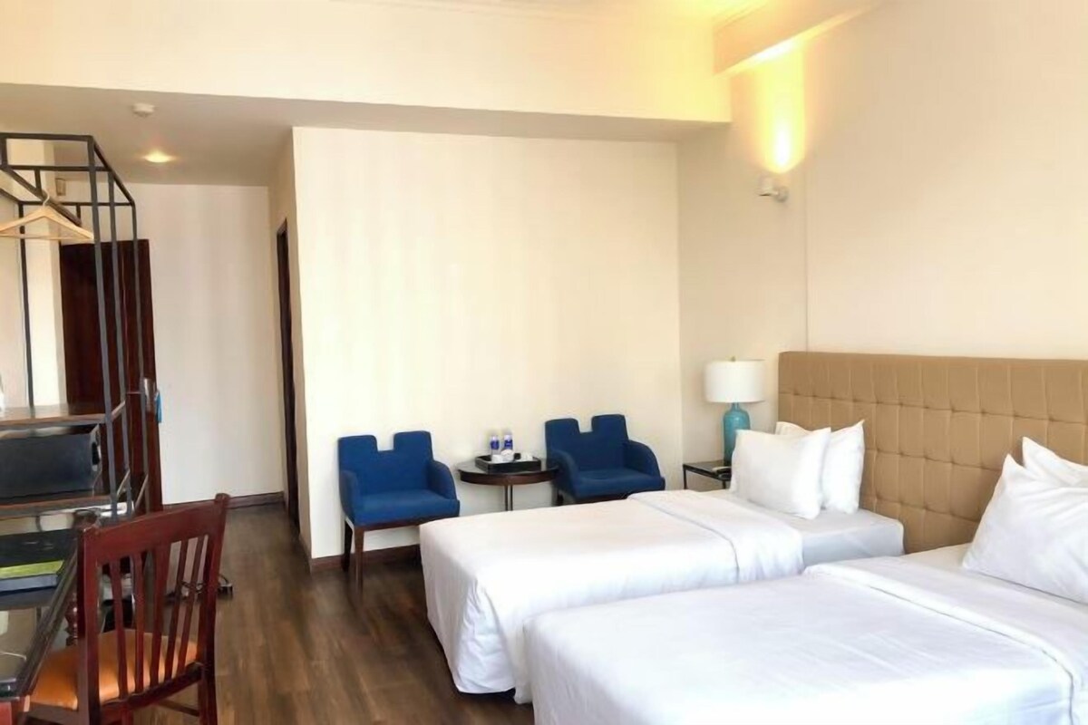 Habitación de hotel con dos camas, un escritorio con silla y una mesita con dos sillas.