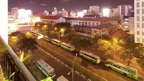 Un paisaje urbano nocturno con varios autobuses verdes en una calle, rodeado de edificios y farolas.