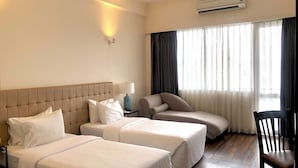 Una habitación de hotel con dos camas, una silla, un escritorio y un aire acondicionado.