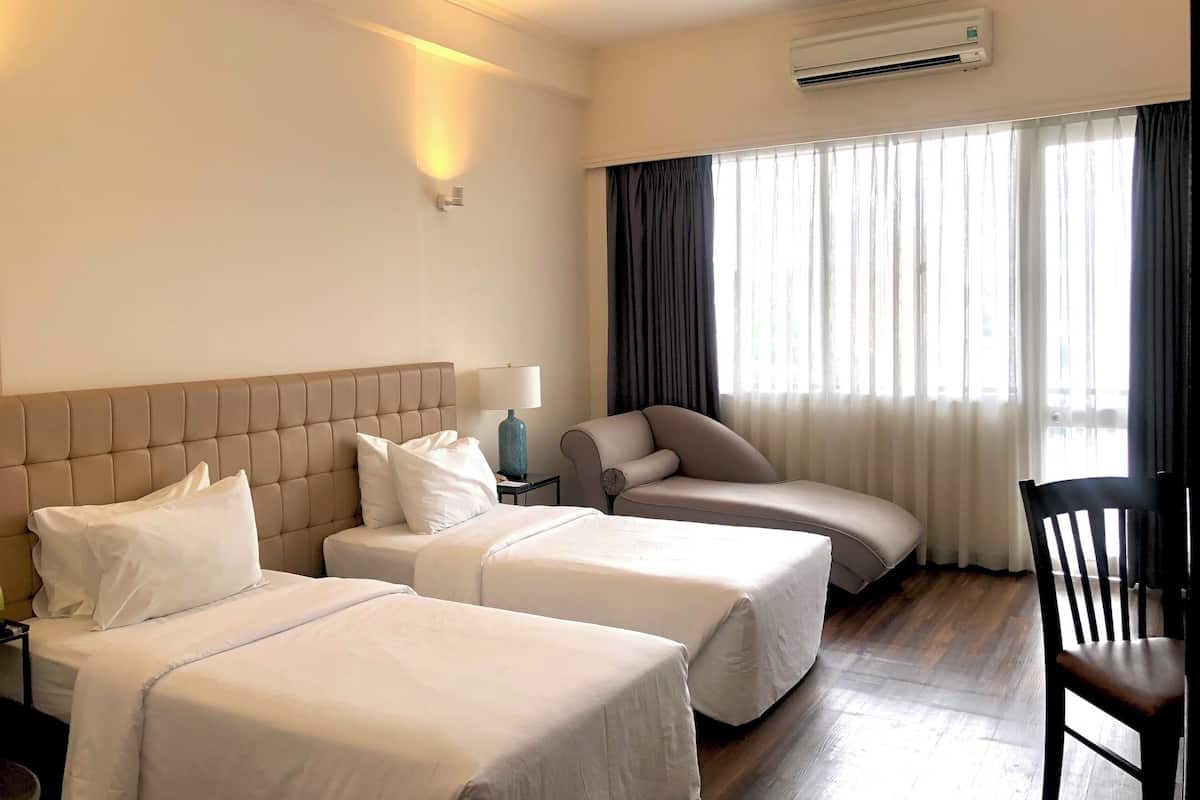 Hotellihuone, jossa on kaksi sänkyä, tuoli, työpöytä ja ilmastointilaite.