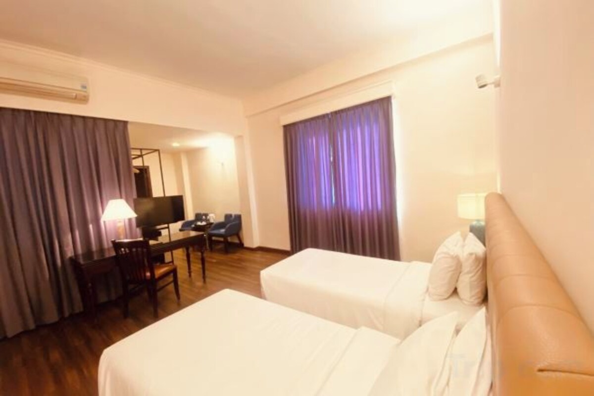 Een hotelkamer met twee bedden, een bureau, een stoel, een televisie en gordijnen.