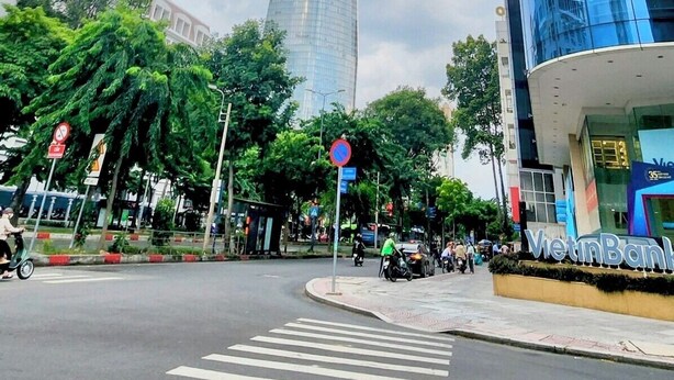 Una calle urbana moderna con un edificio de cristal destacado, un paso de peatones y zonas verdes circundantes.