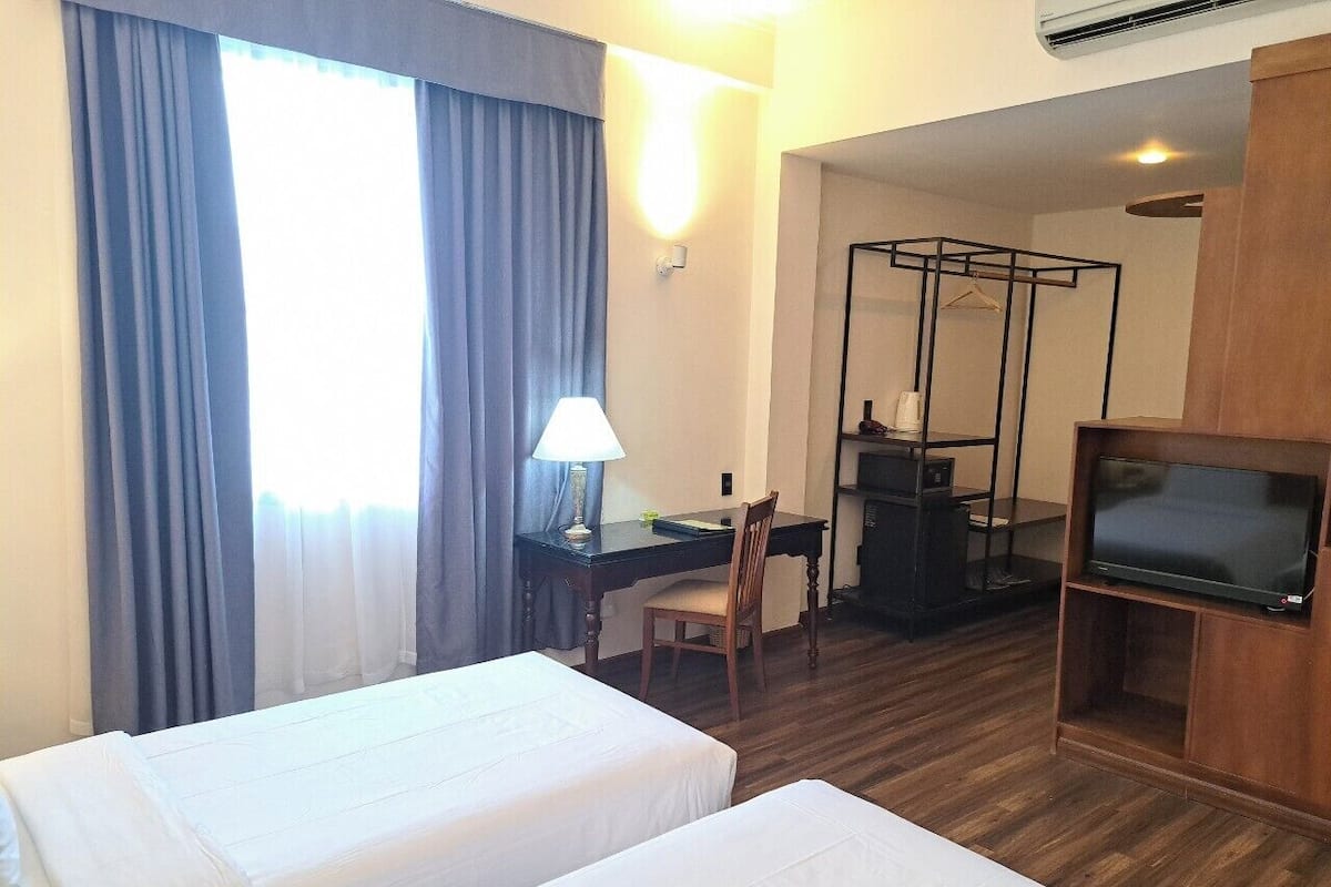 Hotellihuone, jossa on kaksi sänkyä, työpöytä tuolilla, televisio ja vaatekaappi.