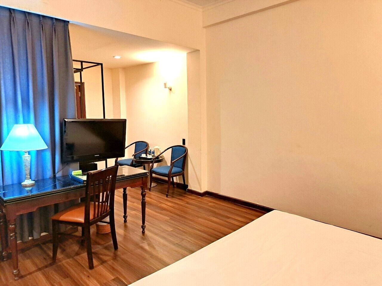 Et hotelværelse med fjernsyn, et skrivebord med lampe, to stole og en seng.