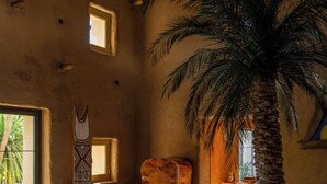 Een ruime woonkamer met een grote palmboom, een bank, een bijzettafeltje met boeken en een stoel.