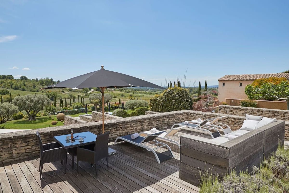A wooden deck with a table and chairs, a large umbrella, and a stone wall.