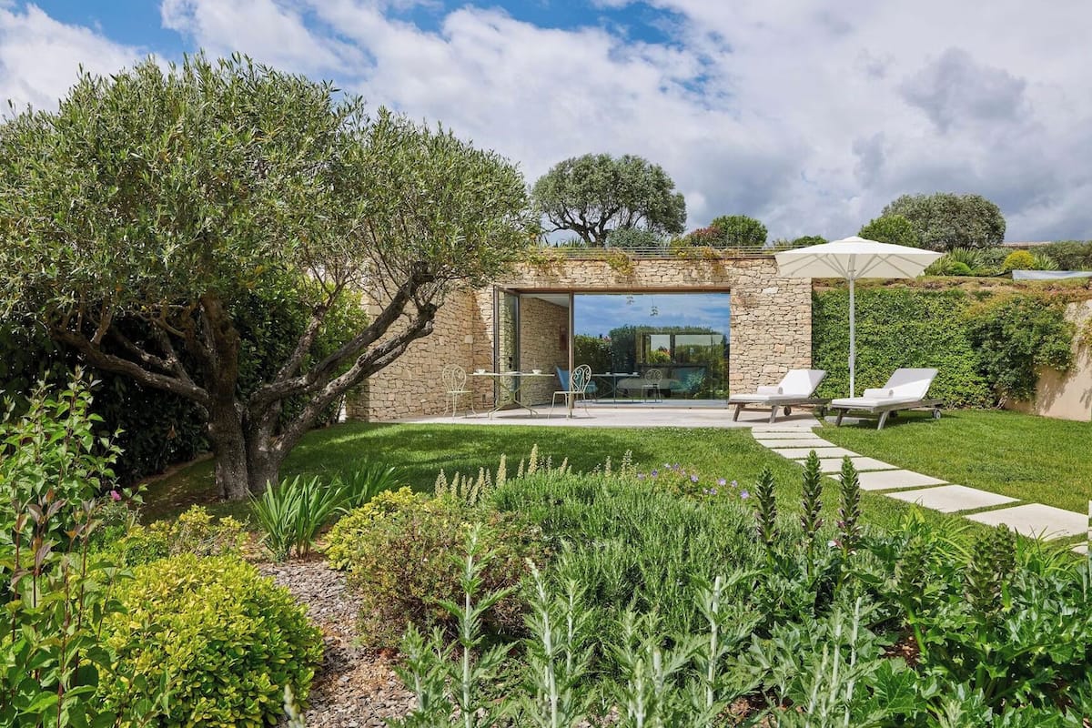 A modern outdoor patio with stone walls, a glass door entrance, and a seating area with two lounge chairs.
