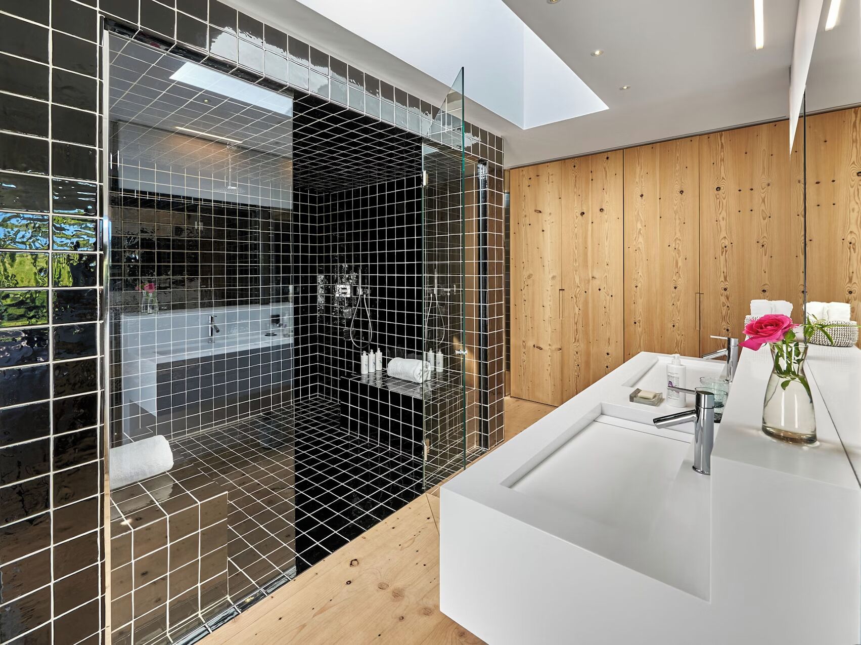 Une salle de bain moderne avec une douche à parois de verre, un mur recouvert de panneaux en bois et un lavabo blanc agrémenté d’articles de toilette.