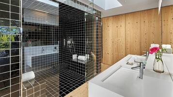 Une salle de bain moderne avec une douche à parois de verre, un mur recouvert de panneaux en bois et un lavabo blanc agrémenté d’articles de toilette.