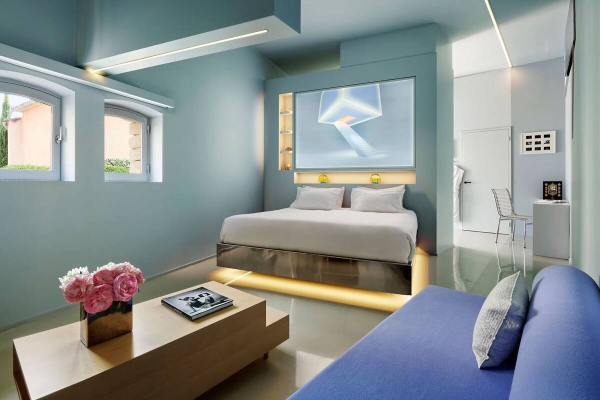 Een moderne slaapkamer met een bed, nachtkastjes, een bank en een groot raam.