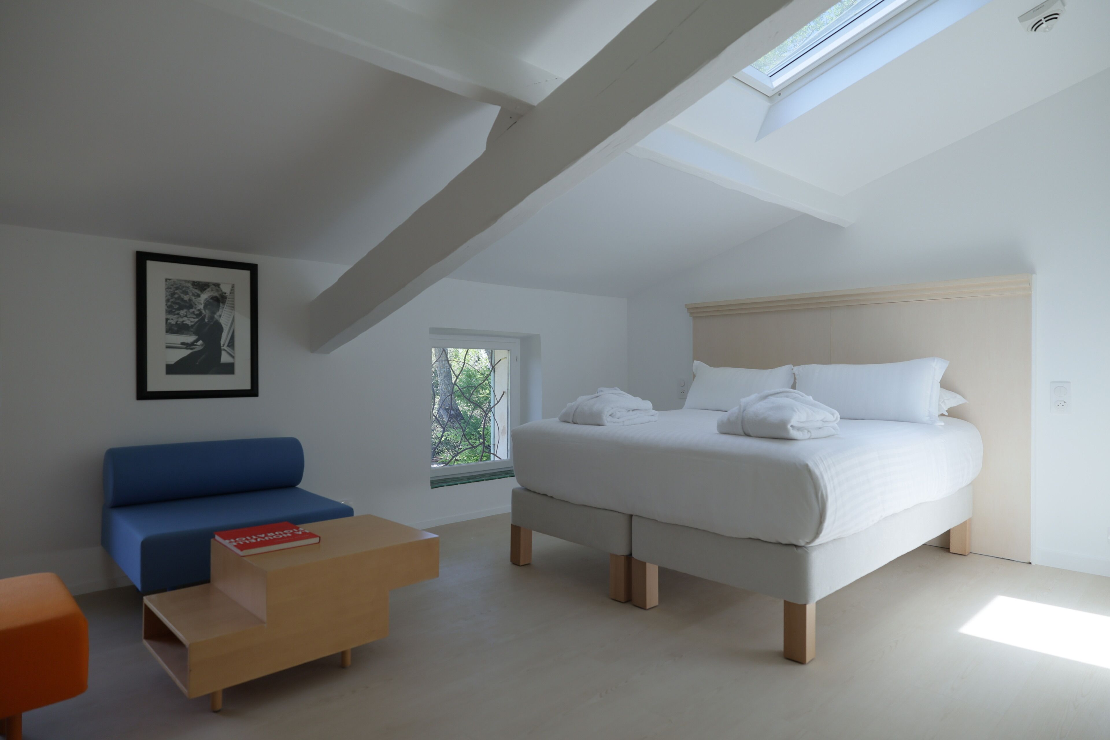 A bedroom with a bed, a blue sofa, a wooden coffee table, and a framed picture on the wall.