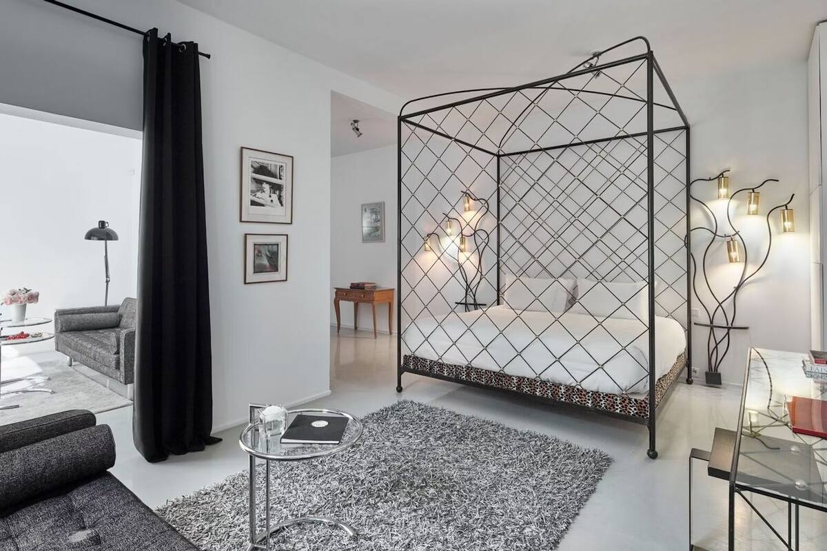 Een moderne slaapkamer met een geometrisch bedbaldakant, een glazen bijzettafeltje en een minimalistische inrichting.