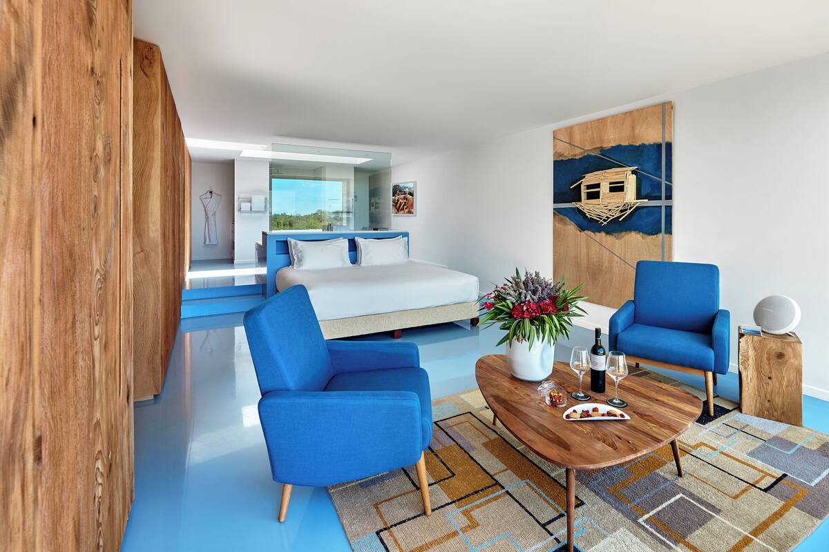 Een moderne woonkamer met een bank, twee blauwe fauteuils, een bijzettafeltje met drankjes en een schilderij aan de muur.