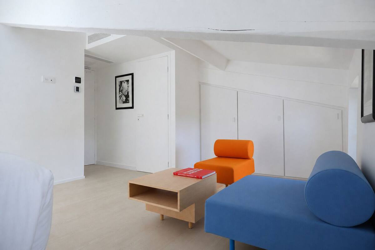Een moderne, minimalistische kamer met een blauwe bank, een oranje fauteuil en een houten salontafel.