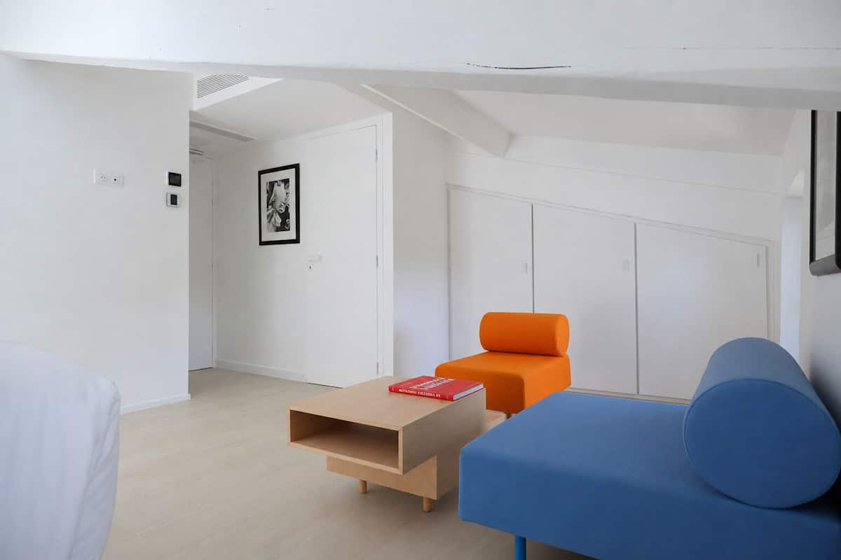 A modern, minimalistic room with a blue sofa, an orange chair, and a wooden coffee table.
