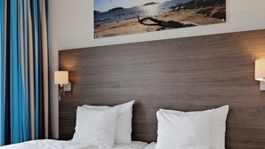 A hotel room with a large bed, a headboard with a picture of a beach, and two bedside lamps.