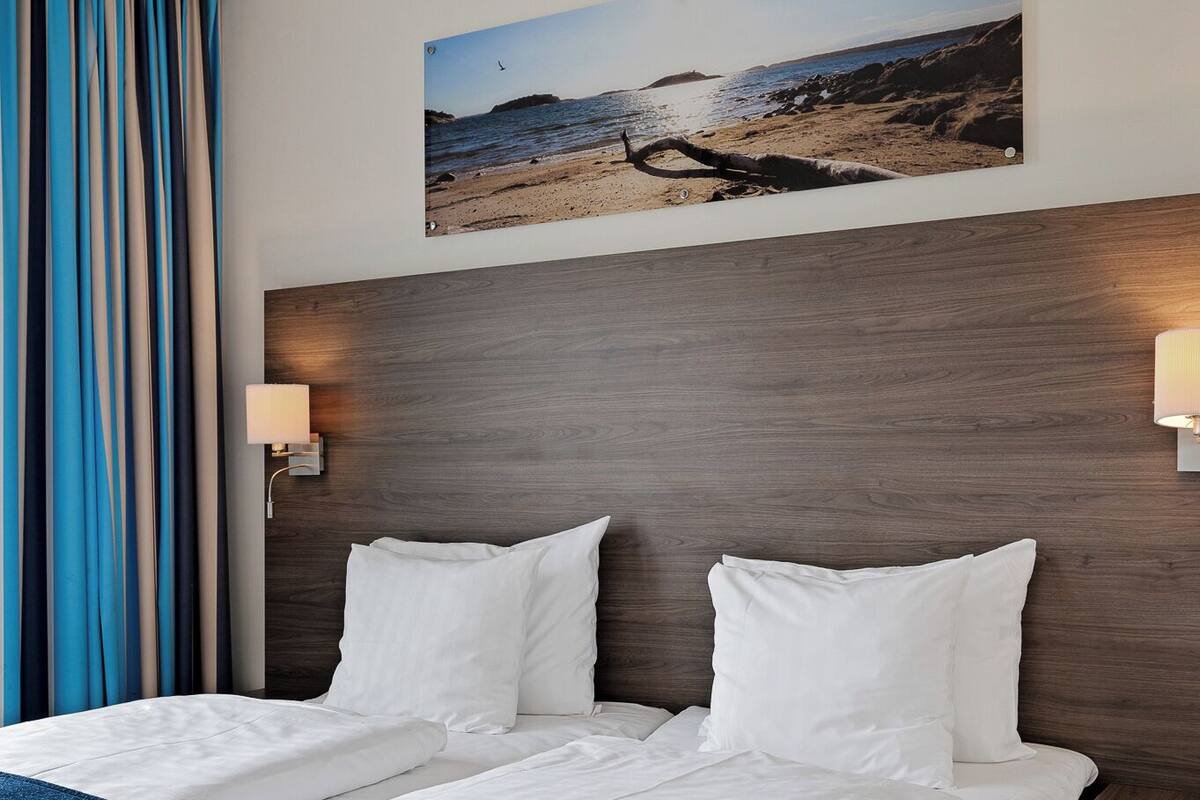 A hotel room with a large bed, a headboard with a picture of a beach, and two bedside lamps.