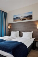 Una habitación de hotel con una cama grande, cabecera con una imagen de una playa y dos lámparas de noche.