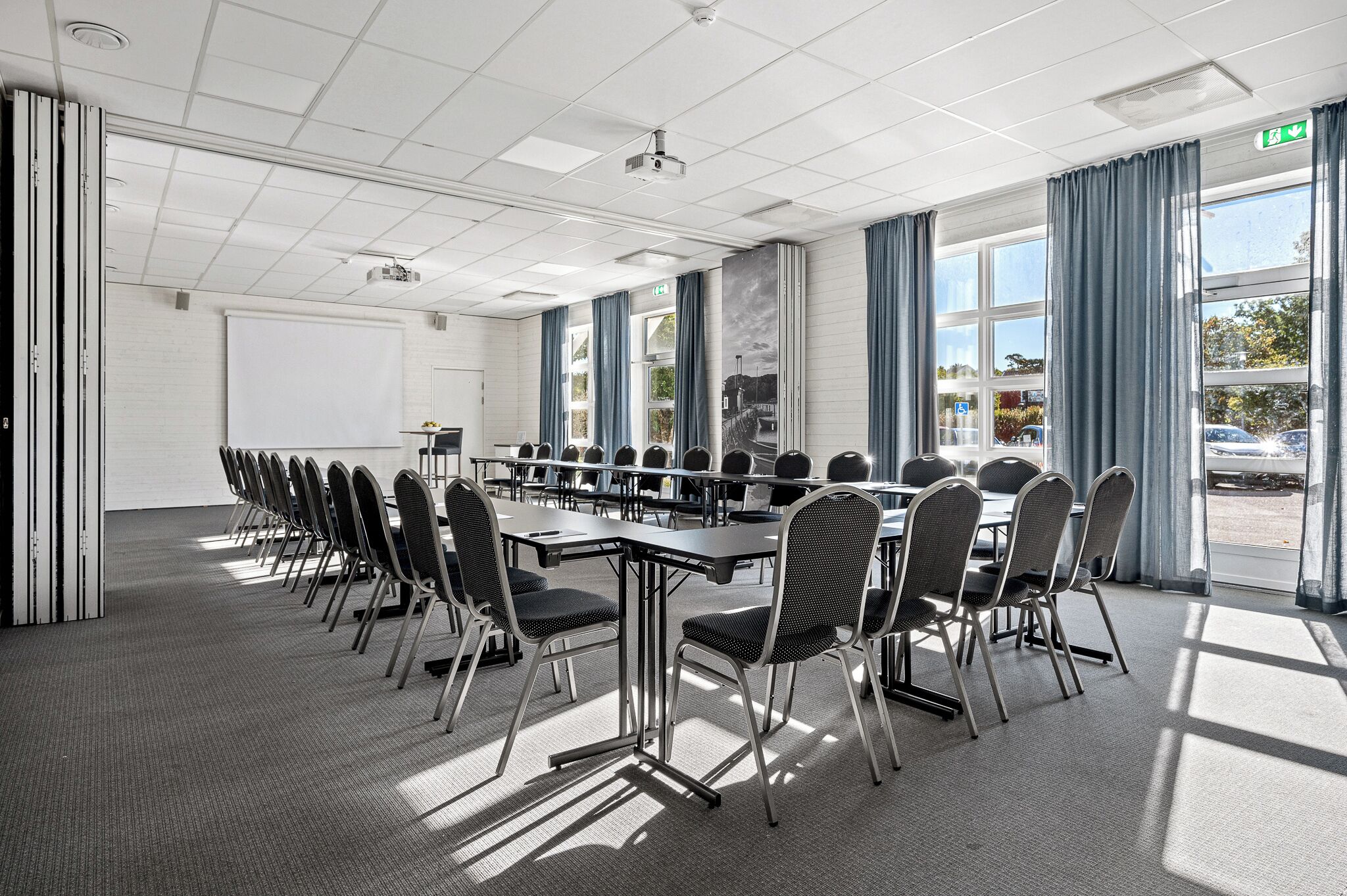 A conference room with a long table, chairs, a projector, and large windows with curtains.
