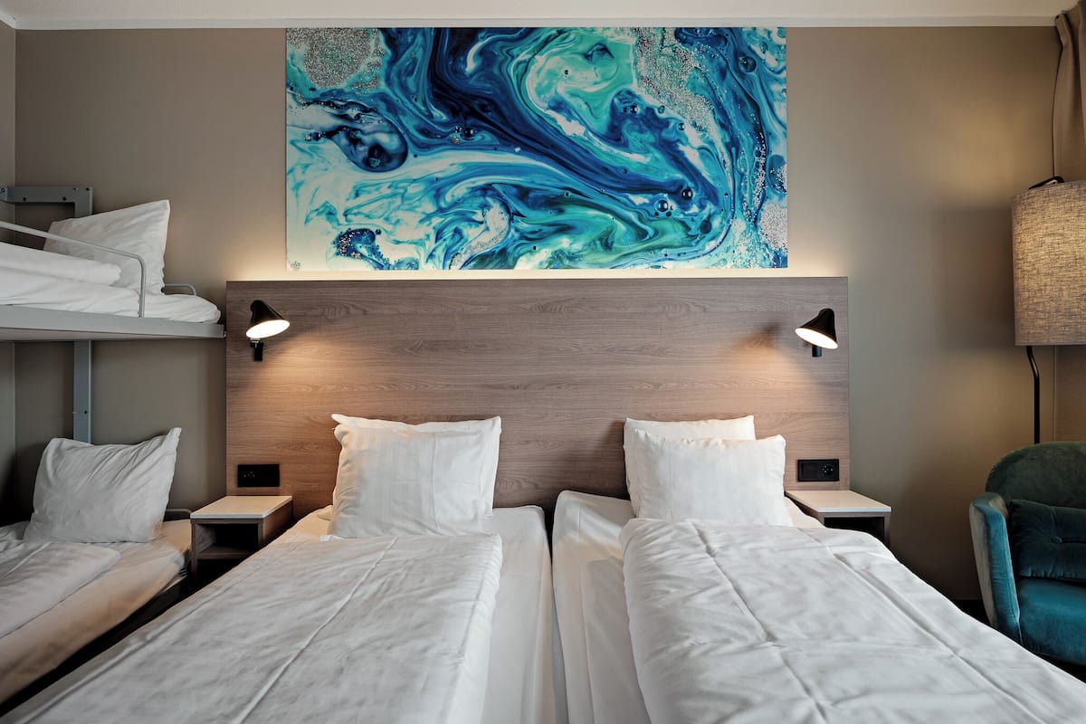 A hotel room with two beds, a wooden headboard, and a large abstract painting above.