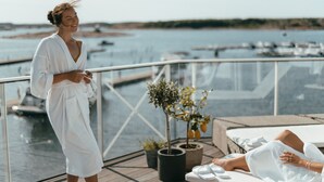 A woman in a white robe on a balcony overlooking a marina with boats. - TanumStrand (Grebbestad)