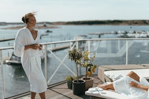 A woman in a white robe on a balcony overlooking a marina with boats. - TanumStrand (Grebbestad)
