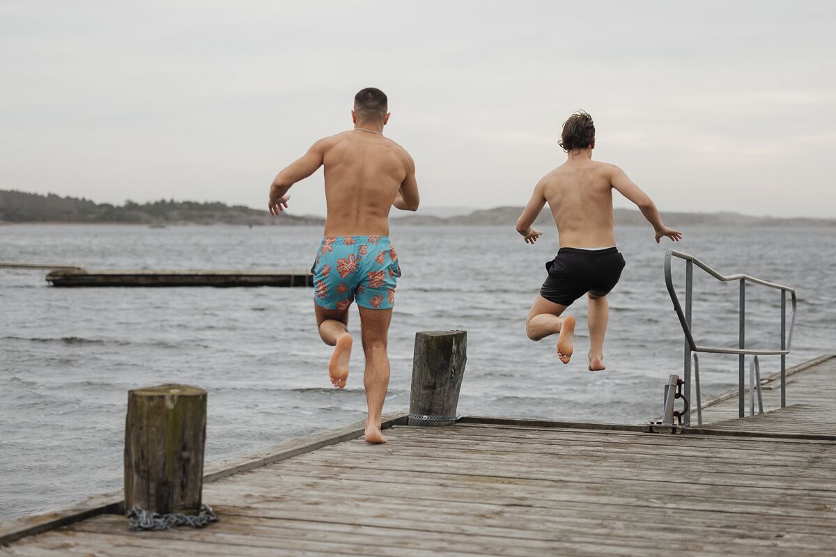 Dos personas saltando desde un muelle de madera al agua.