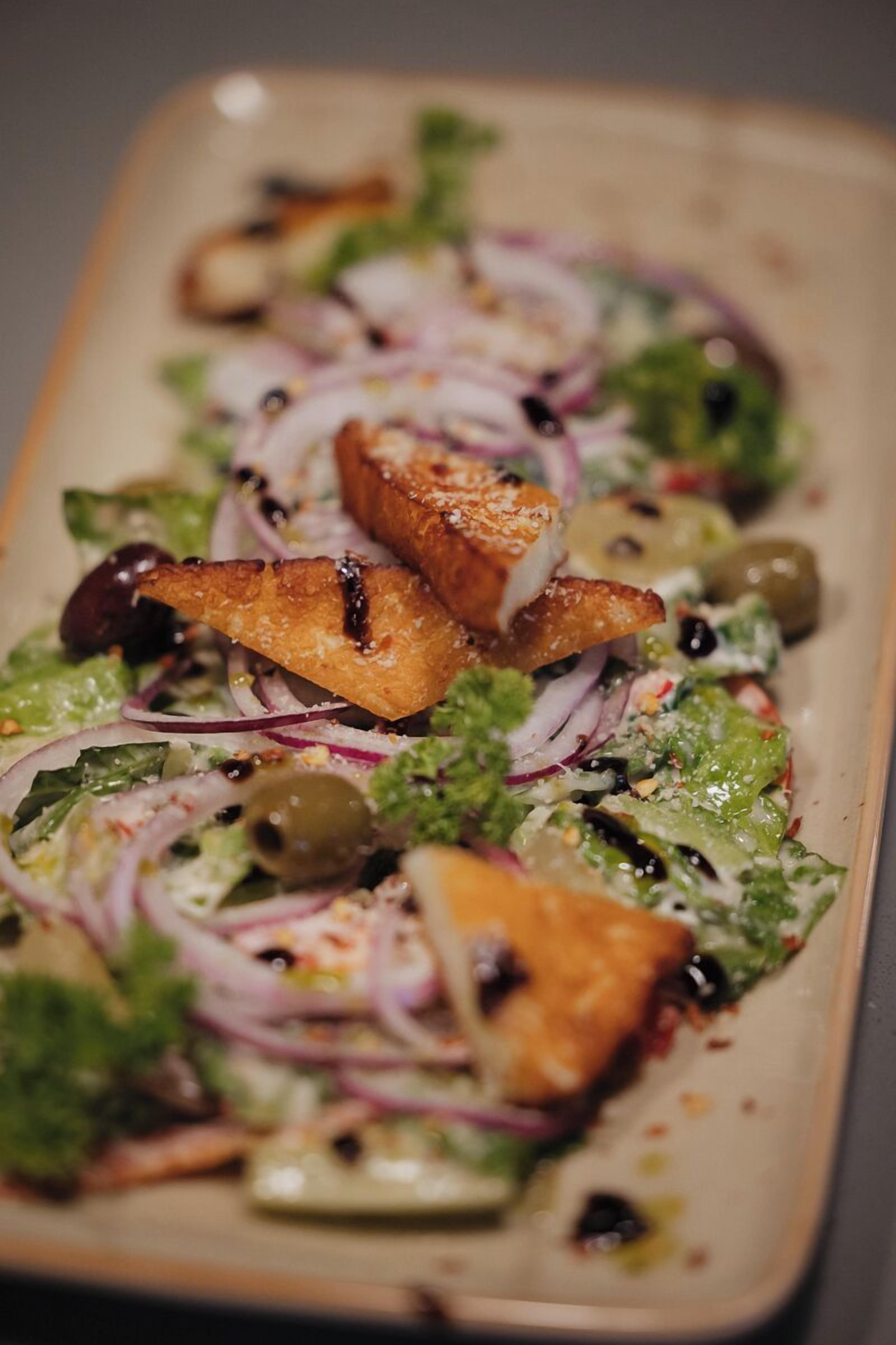 Un plato rectangular con ensalada de lechuga, cebolla morada, aceitunas y trozos de pollo a la parrilla.